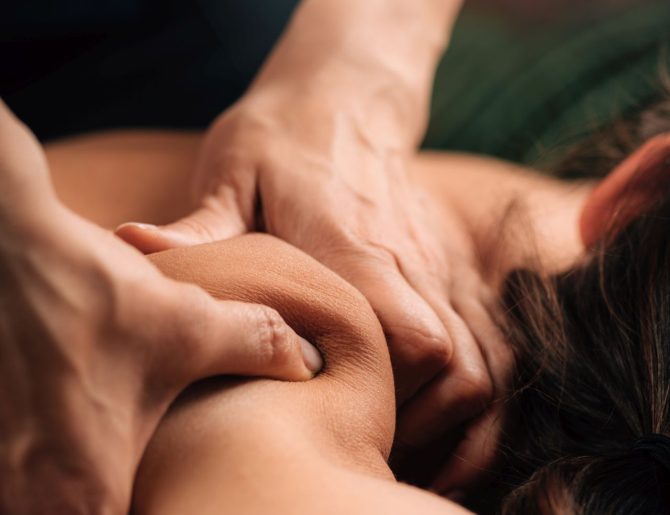 Deep tissue massaging therapy. Therapist hands massaging woman’s shoulder